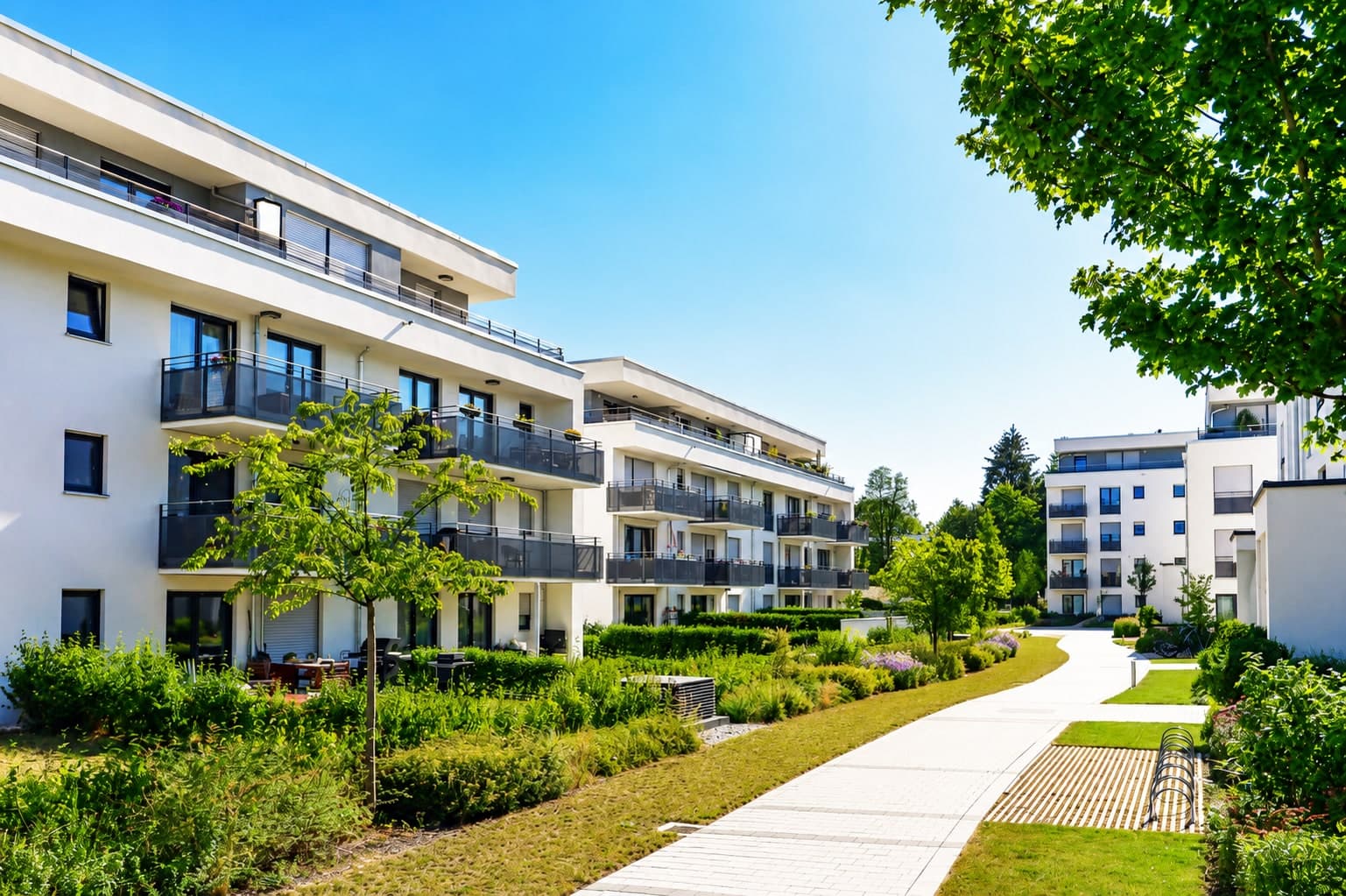 A row of modern low-rise apartment blocks along a landscaped path, each building distinct